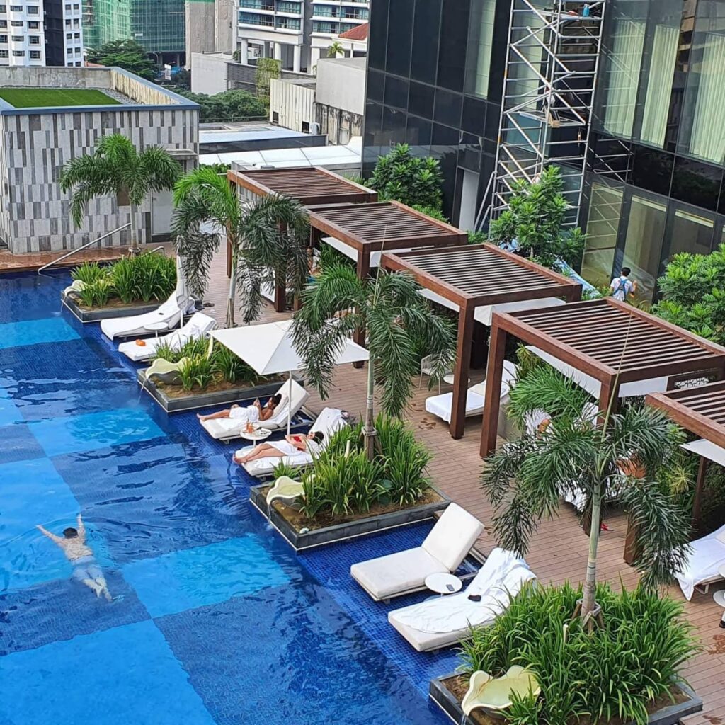 Four Seasons Hotel Kuala Lumpur pool deck with stunning views of Petronas Twin Towers, families enjoying poolside amenities, and lush tropical landscaping