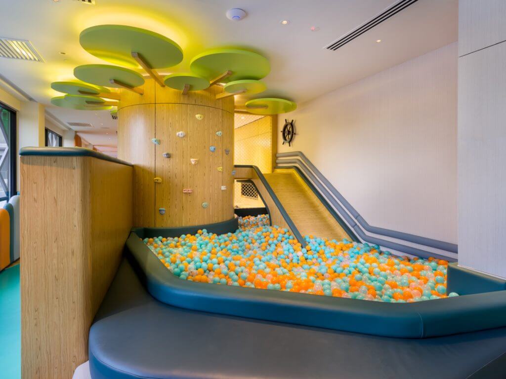 M Resort Kuala Lumpur spacious indoor kids' playroom featuring colorful slide, ball pit, climbing wall panels, and children engaged in play activities