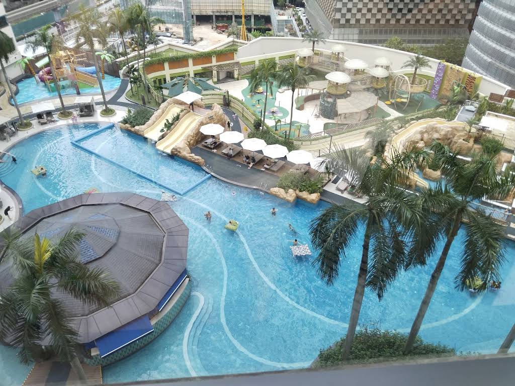 Four Points by Sheraton Kuala Lumpur water park featuring multiple colorful water slides, splash zones, and families enjoying the pool facilities with KLCC skyline in background